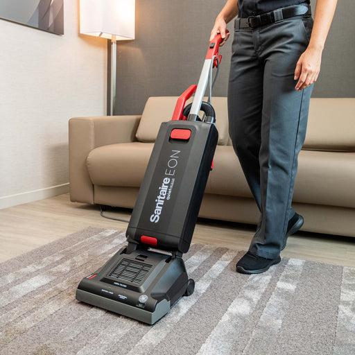 A person vacuuming a carpet on top of a hard floor in a hotel room using the Sanitaire EON SC5500B commercial grade vacuum